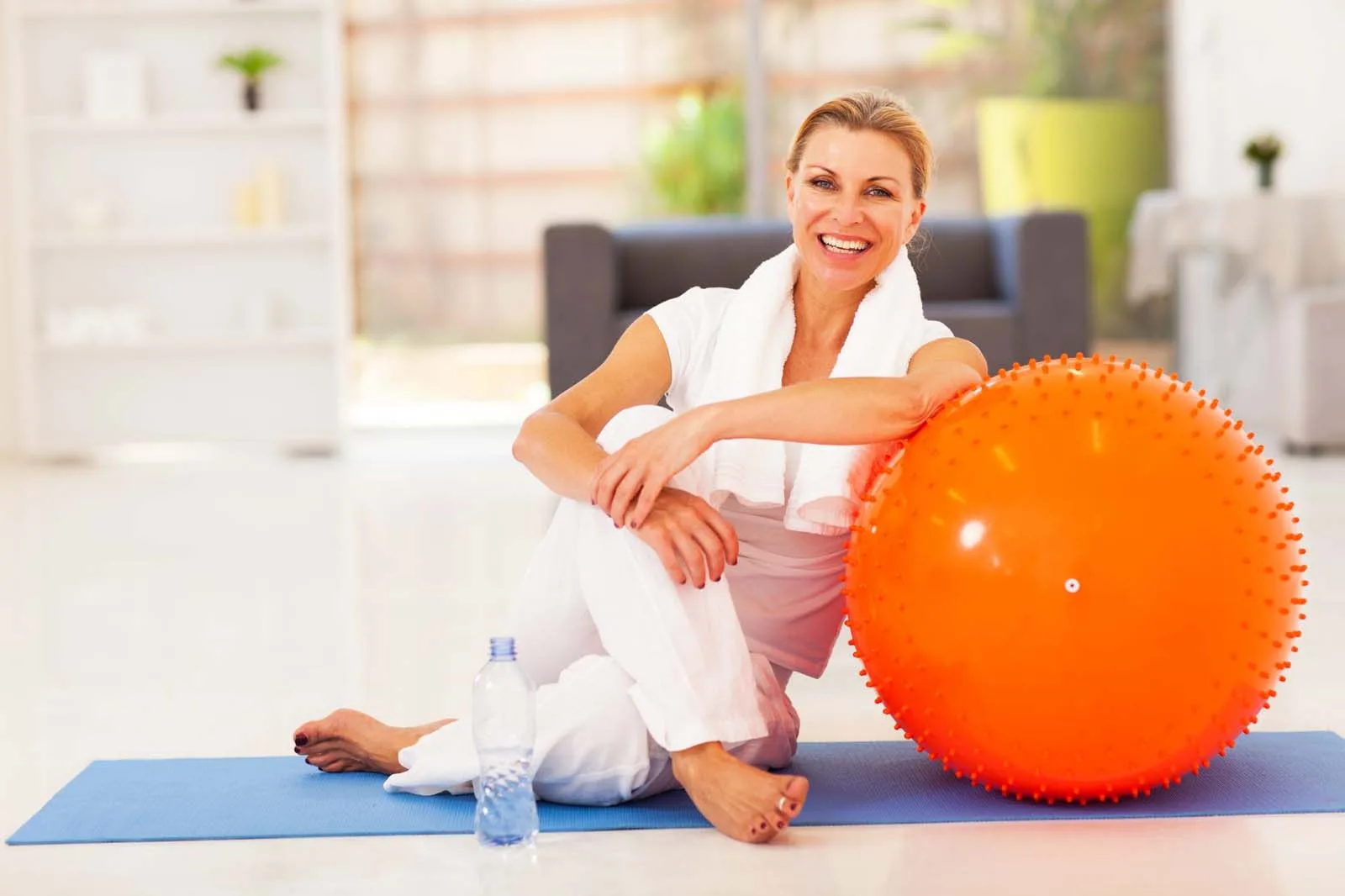 Mujer haciendo yoga con una pelota naranja sobre una colchoneta azul
